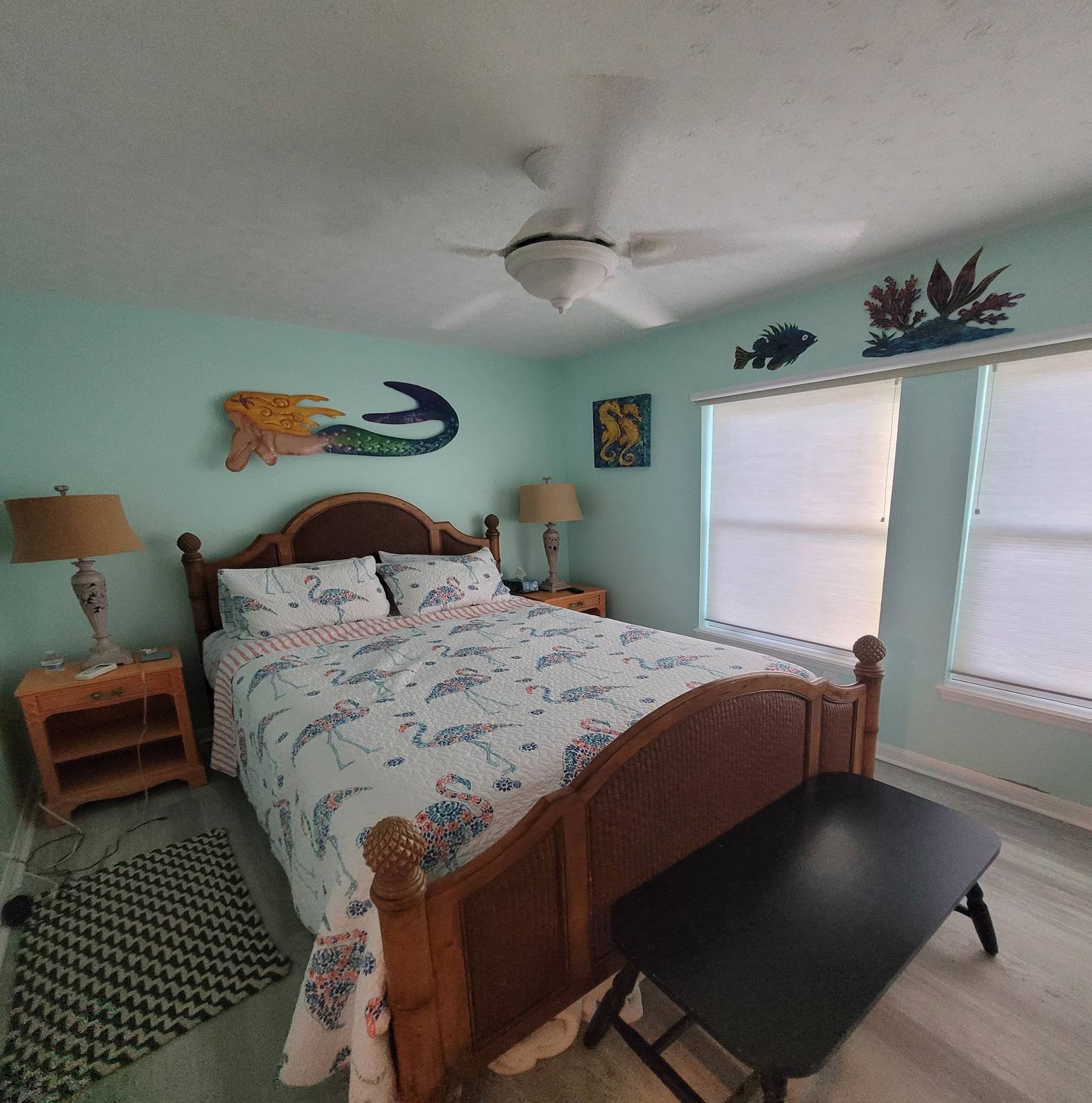 A bedroom with a wicker headboard, flamingo-print bedding, and mermaid wall art