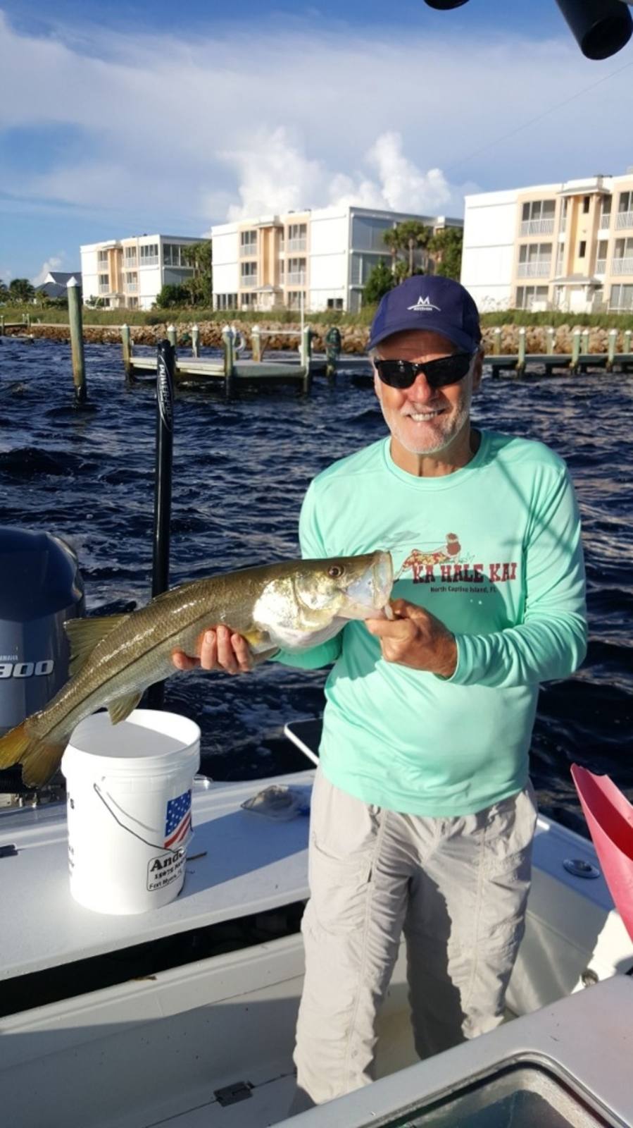 A guest wearing a Ka Hale Kai shirt holding a snook caught from a boat