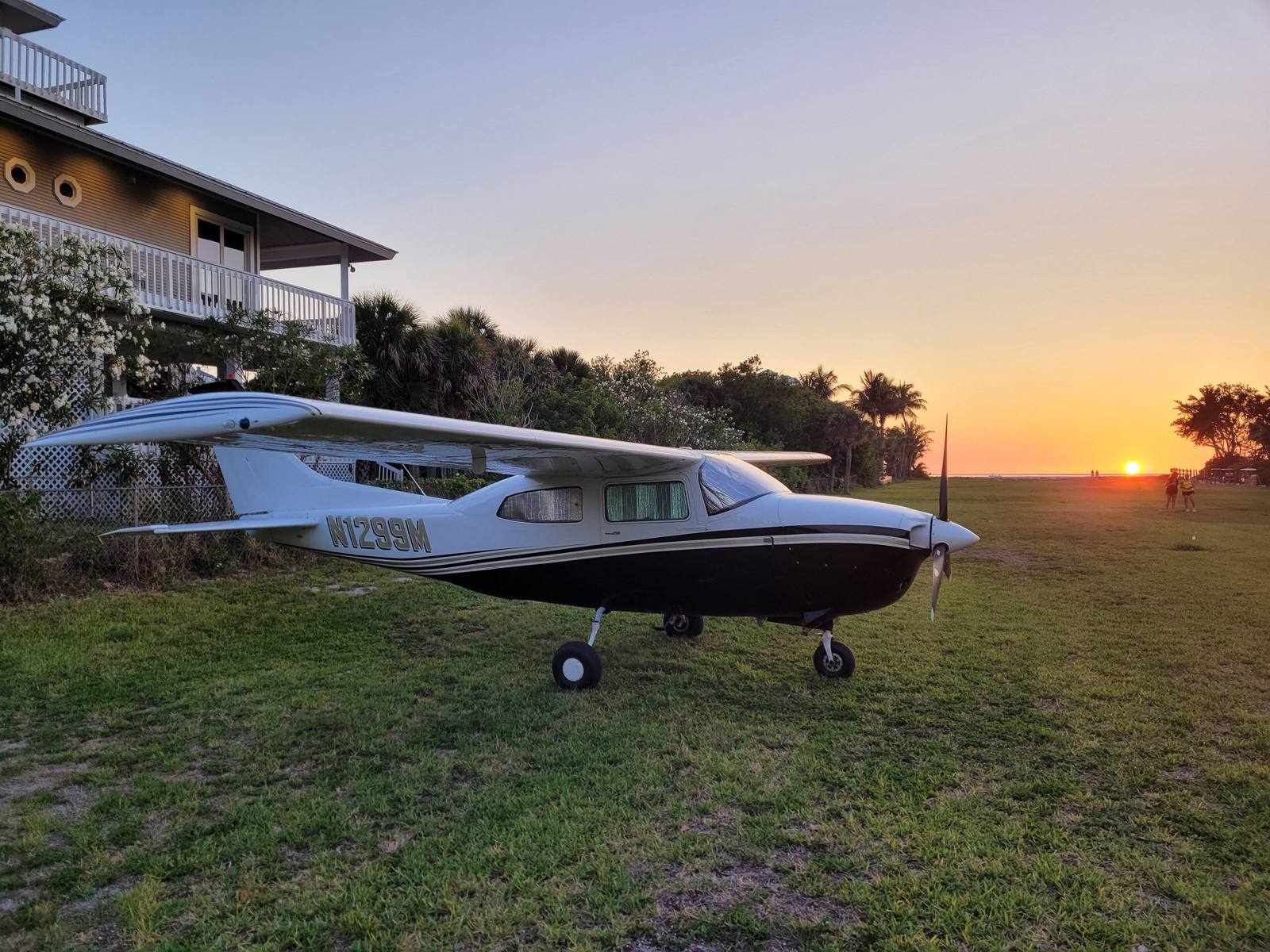 A small plane parked on the grass airstrip near the house at sunset