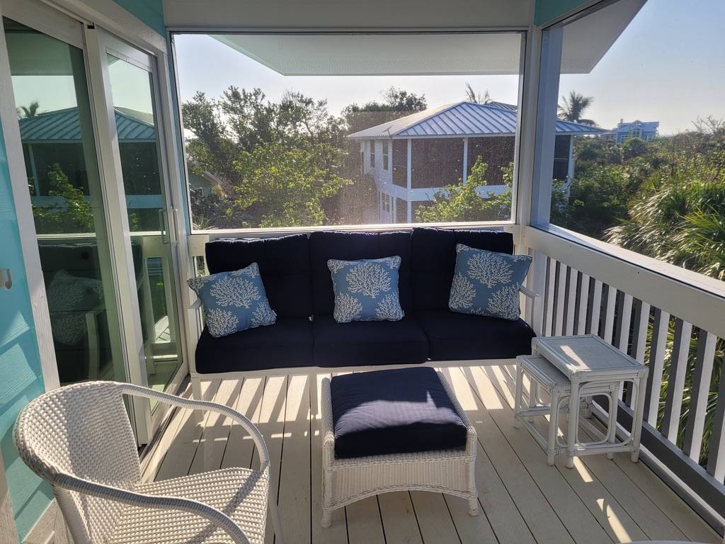 Screened porch with a navy outdoor sofa and coral-print pillows