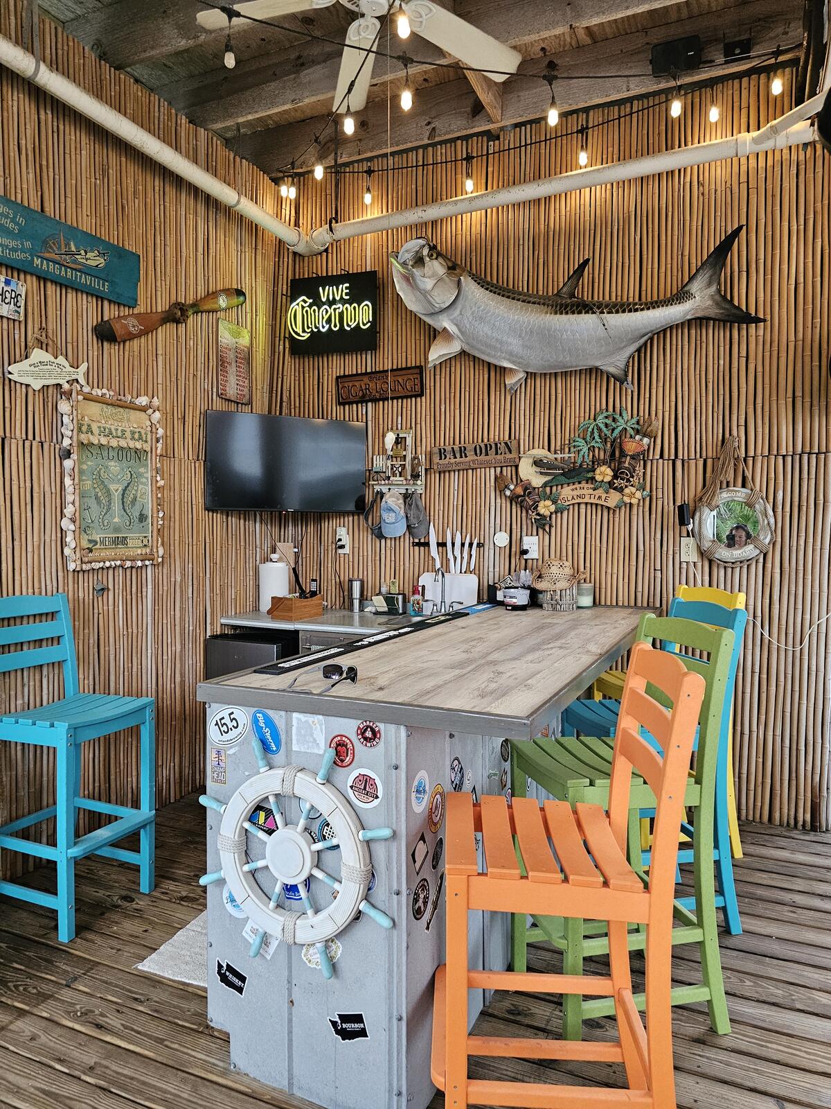 The Ka Hale Kai Saloon: a bamboo-walled poolside bar with a mounted tarpon, string lights, and painted barstools