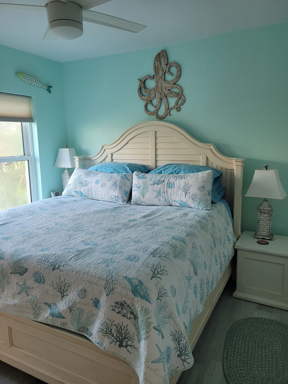 The king master bedroom with a whitewashed headboard, turquoise walls, and driftwood octopus art