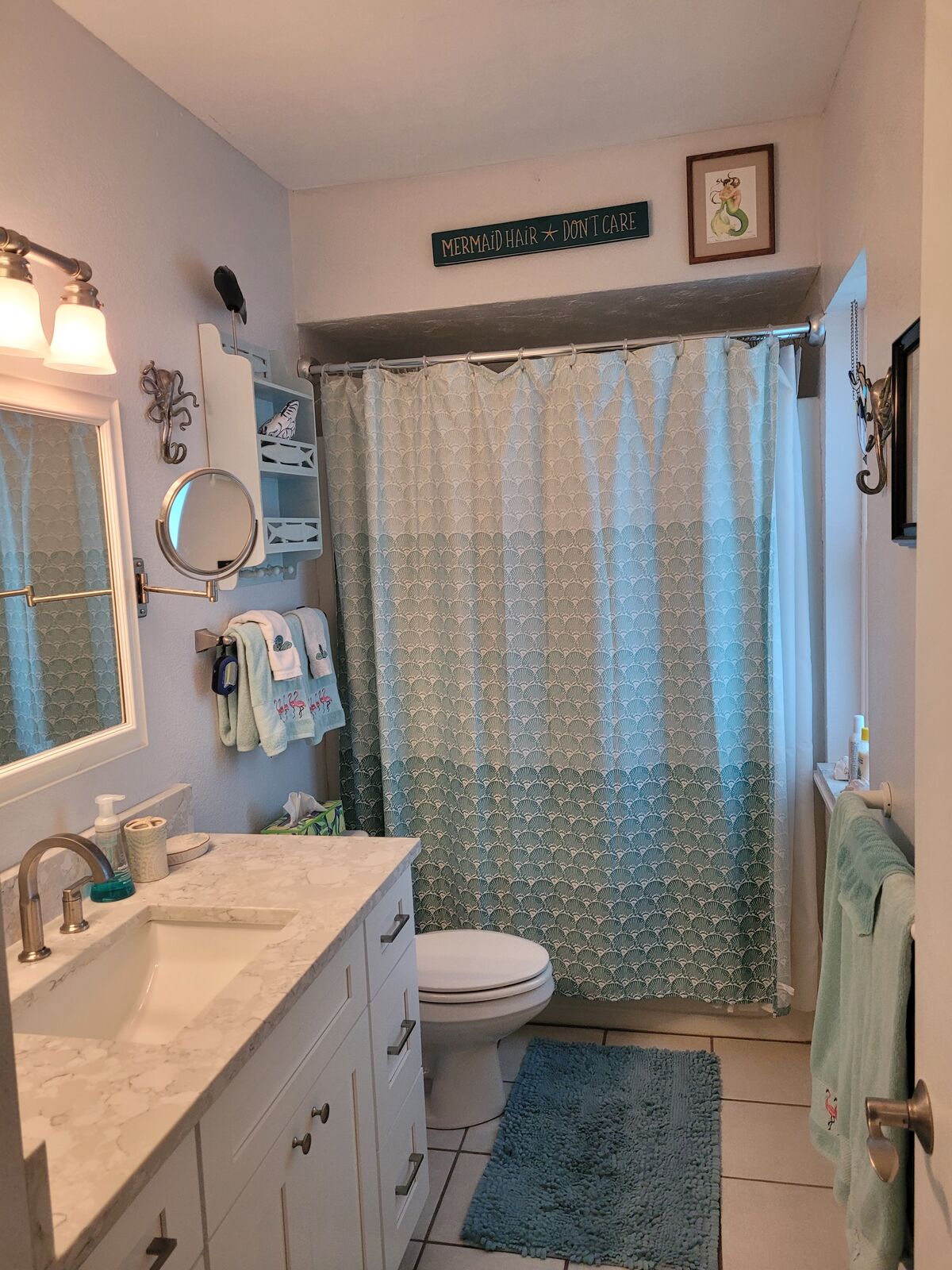A full bath with a quartz vanity, scalloped shower curtain, and a Mermaid Hair Don't Care sign
