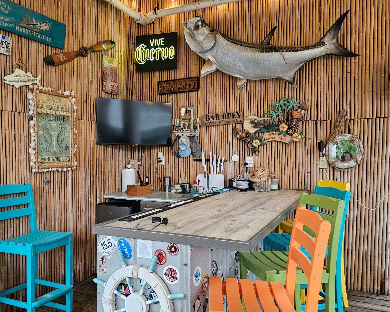 The bar counter under a mounted tarpon, with painted barstools and a Ka Hale Kai Saloon sign